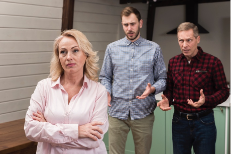 A woman stands with arms crossed, looking away while two men behind her appear to argue or express frustration, symbolizing emotional tension and triangulation in a relationship.